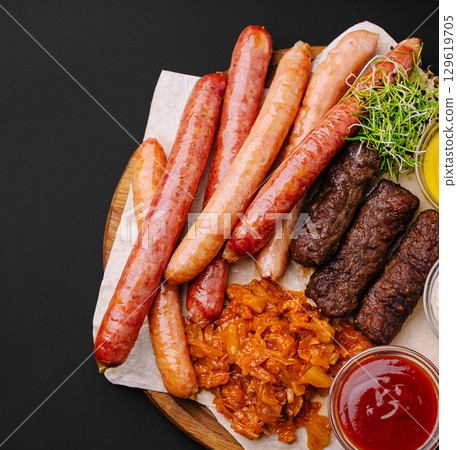 Grilled sausages and meats served with sides on a wooden board Grilled sausages and meats served with sides on a wooden board 129619705