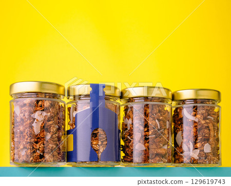 Jars filled with granola and nuts against a bright yellow background 129619743
