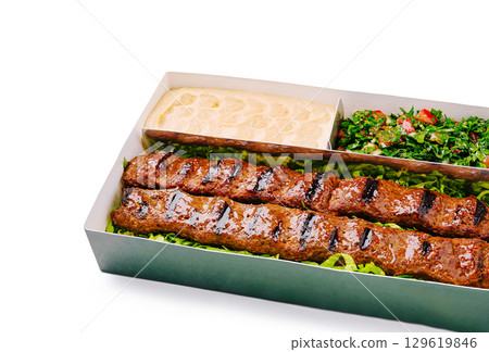 Grilled kebabs served with fresh salad and tahini in a takeout box 129619846