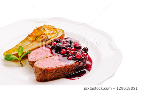 Gourmet dish featuring duck breast with berry sauce and roasted pear garnish 129619851
