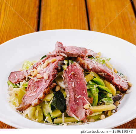 Freshly made salad with grilled meat and nuts on a wooden table 129619877