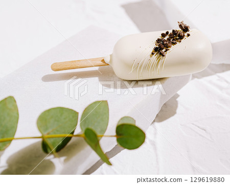 Ice cream treat on a minimalist setting with green foliage accents 129619880