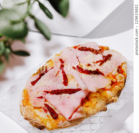 Delicious flatbread topped with ham and sun-dried tomatoes on a white surface Delicious flatbread topped with ham and sun-dried tomatoes on a white surface 129619881