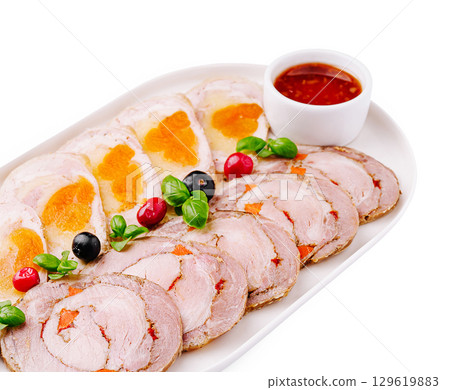Delicious platter of rolled meats with a variety of garnishes and sauce 129619883