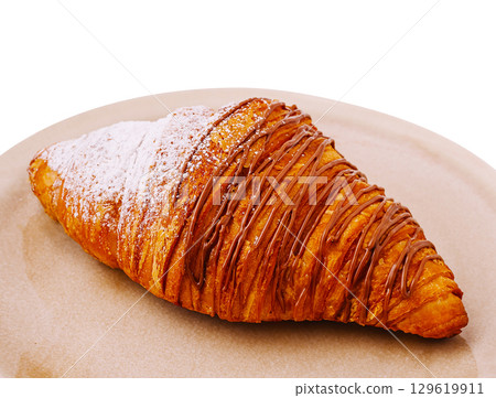 Freshly baked croissant topped with chocolate drizzle and powdered sugar 129619911