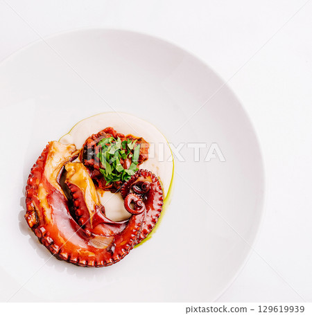 Delicious seafood dish featuring octopus with sauce and herbs on white plate 129619939
