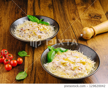 Delicious pasta served in bowls with cherry tomatoes and basil on wooden table Delicious pasta served in bowls with cherry tomatoes and basil on wooden table 129620042