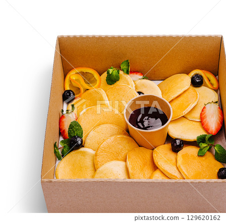 Delicious mini pancakes served with fruit and syrup in a takeout box 129620162