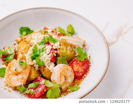 Shrimp and vegetable dish served in a bowl with fresh herbs and toppings 129620177