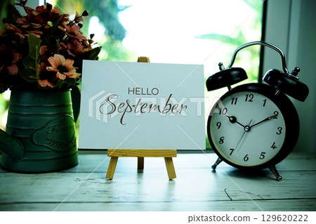 Hello September text on paper card with easel and alarm clock in the window background 129620222