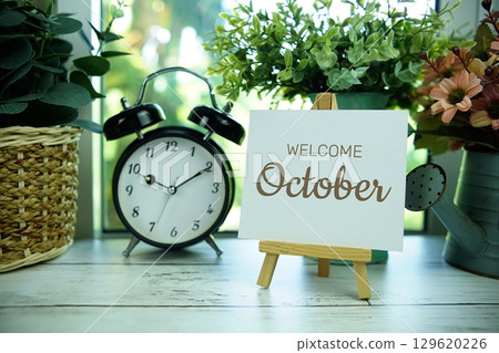 Welcome October text on paper card with easel and alarm clock in the window background Welcome October text on paper card with easel and alarm clock in the window background 129620226