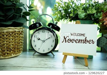 Welcome November text on paper card with easel and alarm clock in the window background 129620227