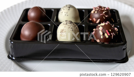 Chocolate-coated marshmallow treats in box on white plate table 129620907