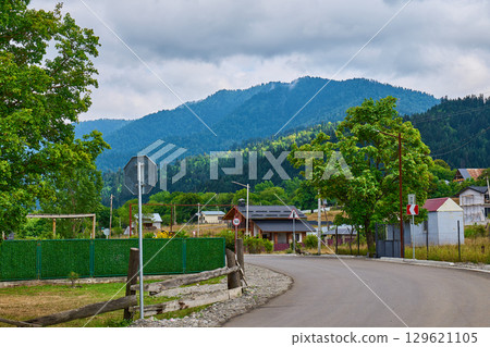 A winding road in a tranquil rural area surrounded by lush trees and distant mountains A winding road in a tranquil rural area surrounded by lush trees and distant mountains 129621105