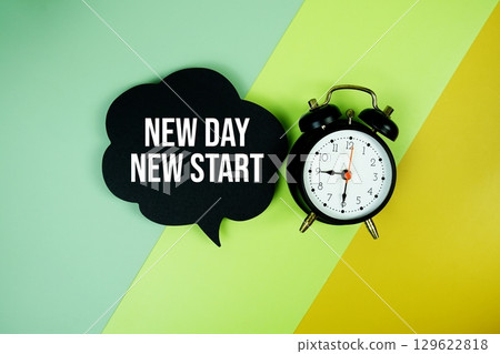 New Day New Start text on speech bubble with alarm clock top view on green and yellow geometric background New Day New Start text on speech bubble with alarm clock top view on green and yellow geometric background 129622818