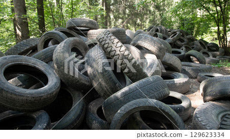 Discarded tires accumulate in a forested area, illustrating the serious issue of waste management and environmental pollution. The scene highlights the need for recycling initiatives. 129623334