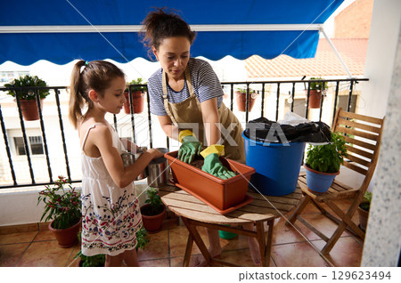 Mother and Daughter Gardening Together on a Sunlit Balcony 129623494