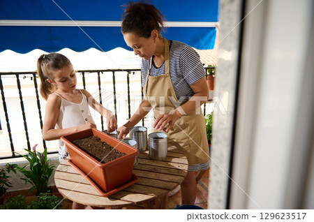 Mother and Daughter Gardening Together on Sunny Balcony Terrace 129623517