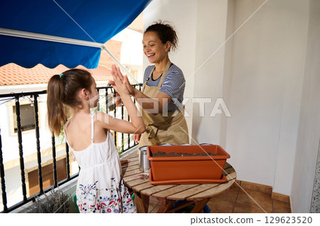 Mother and Daughter Gardening Together on a Sunny Balcony Mother and Daughter Gardening Together on a Sunny Balcony 129623520