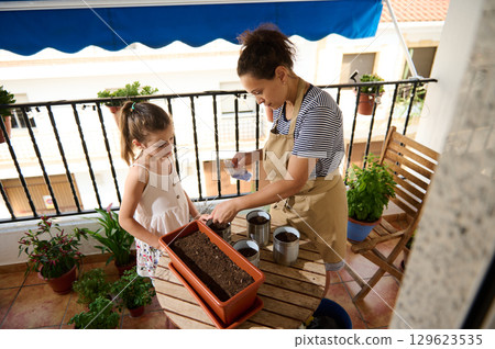 Mother and Daughter Plant Seeds Together on a Cozy Balcony Mother and Daughter Plant Seeds Together on a Cozy Balcony 129623535