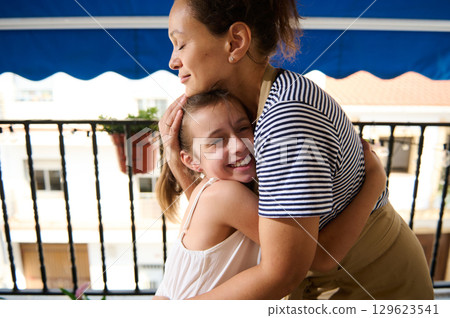Mother and Daughter Sharing a Heartwarming Hug on a Sunny Balcony 129623541