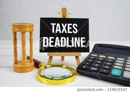 Taxes Deadline text with magnifying glass and calculator on wooden background 129623547