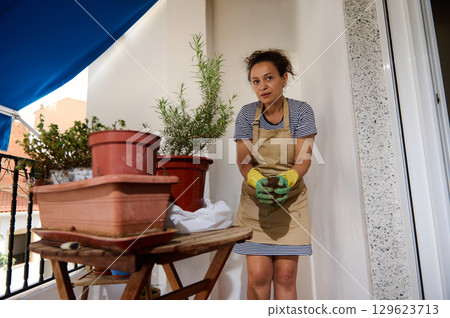 Woman Gardening on Balcony with Potted Plants and Protective Gloves Woman Gardening on Balcony with Potted Plants and Protective Gloves 129623713