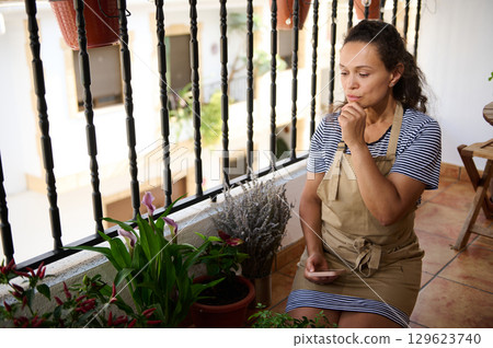 Woman Sitting on Balcony Reflecting Amidst Decorative Plants and Flowers 129623740