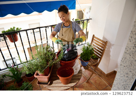 Woman Gardening on Balcony With Pots and Plants in Urban Setting 129623752