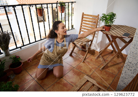 Woman Gardening on Balcony Surrounded By Potted Plants and Wooden Furniture Woman Gardening on Balcony Surrounded By Potted Plants and Wooden Furniture 129623772