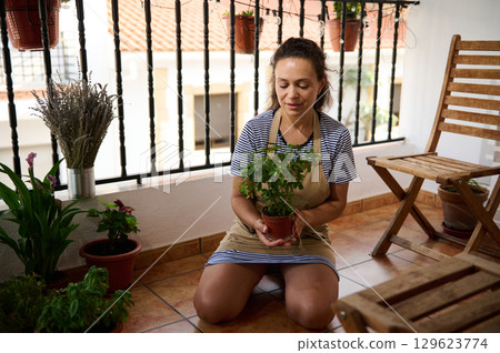 Woman Gardening on Balcony with Potted Plants and Wooden Furniture 129623774