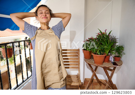 Joyful Woman Gardening on a Sunny Balcony With Potted Plants 129623803