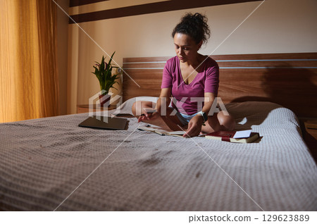 Woman Studying on Bed with Books and Device in Calm Room 129623889