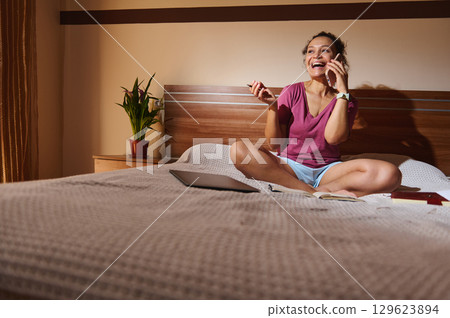 Young Woman Enjoying a Phone Conversation While Relaxing on Her Bed Young Woman Enjoying a Phone Conversation While Relaxing on Her Bed 129623894