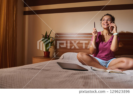 Woman Smiling While Working from Bed, Engaged in a Phone Call 129623896