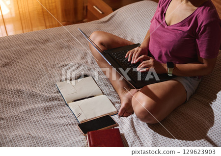 Woman Working on Laptop at Home with Notebooks and Smartphone Nearby 129623903