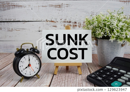 Sunk Cost text with alarm clock and calculator on wooden background 129623947