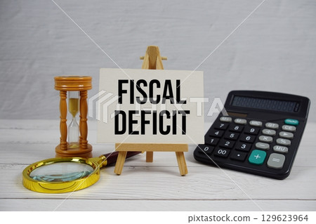 Fiscal Deficit text with magnifying glass and calculator on wooden background 129623964