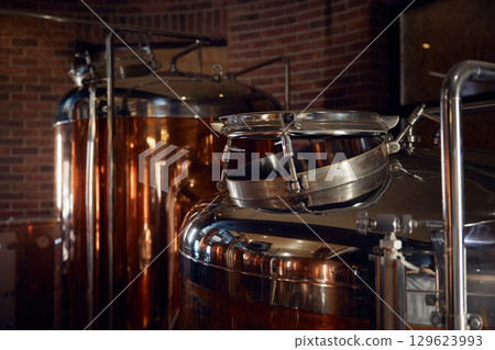 A long row of copper tanks is neatly lined up against a brick wall A long row of copper tanks is neatly lined up against a brick wall 129623993