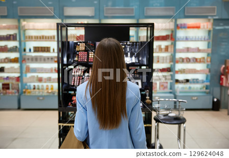 A woman is focused on various makeup products on a shelf 129624048