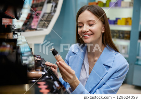 A woman in a blue jacket is browsing makeup items in a store 129624059