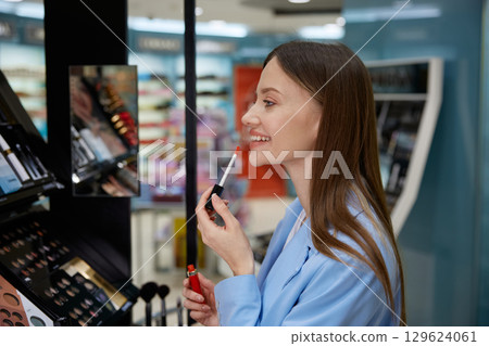 A woman is applying a vibrant shade of lipstick in a cosmetics store 129624061