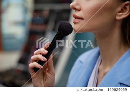A woman in a blue jacket applies makeup with a brush 129624069