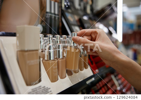 A woman is reaching for a bottle of foundation on a store shelf 129624084