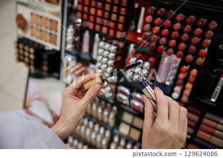 A woman holds a mascara brush in front of a makeup display 129624086