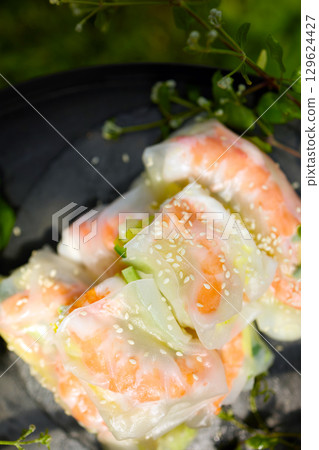 Fresh spring rolls served on a decorative tray surrounded by greenery in a vibrant outdoor setting 129624427