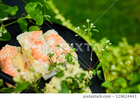 Fresh spring rolls served on a decorative tray surrounded by greenery in a vibrant outdoor setting Fresh spring rolls served on a decorative tray surrounded by greenery in a vibrant outdoor setting 129624441