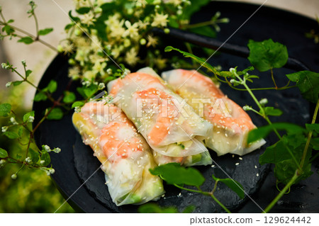 Fresh spring rolls served on a decorative tray surrounded by greenery in a vibrant outdoor setting Fresh spring rolls served on a decorative tray surrounded by greenery in a vibrant outdoor setting 129624442