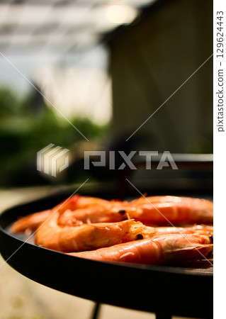 Grilled shrimp on a black grill plate surrounded by green grass in a sunny outdoor setting Grilled shrimp on a black grill plate surrounded by green grass in a sunny outdoor setting 129624443