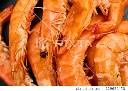 Grilled shrimp on a black grill plate surrounded by green grass in a sunny outdoor setting 129624450